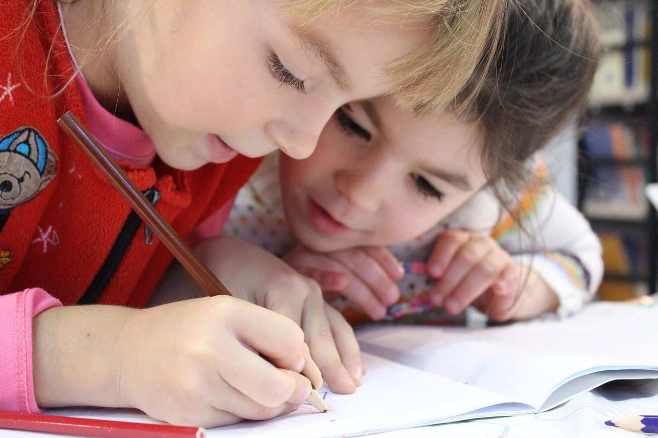 Two children are writing on a piece of paper.